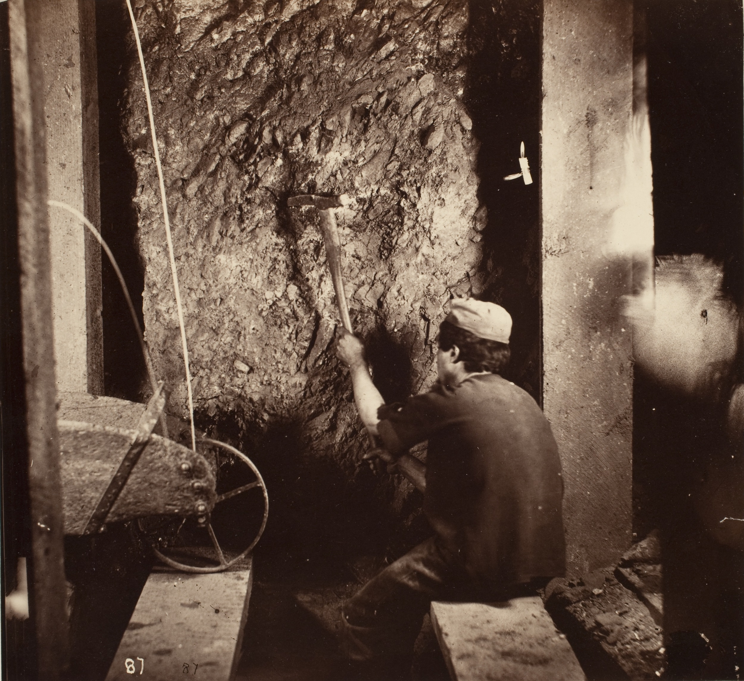 Black-and-white photograph of a worker in a mine using a pickaxe on a rocky wall