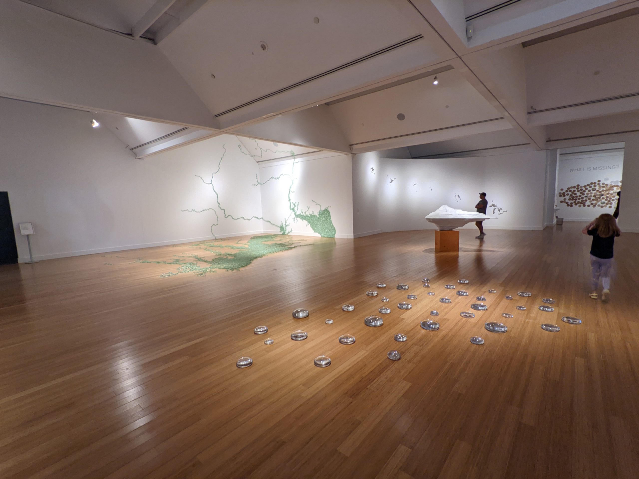 View of museum gallery interior, with several works of art installed. Through a doorway is visible the installation in fig. 1; to the left the installation in fig. 5, and in the center some bubble-shaped forms set directly on the hardwood floor, as well as a white iceberg-shaped sculpture on a pedestal.