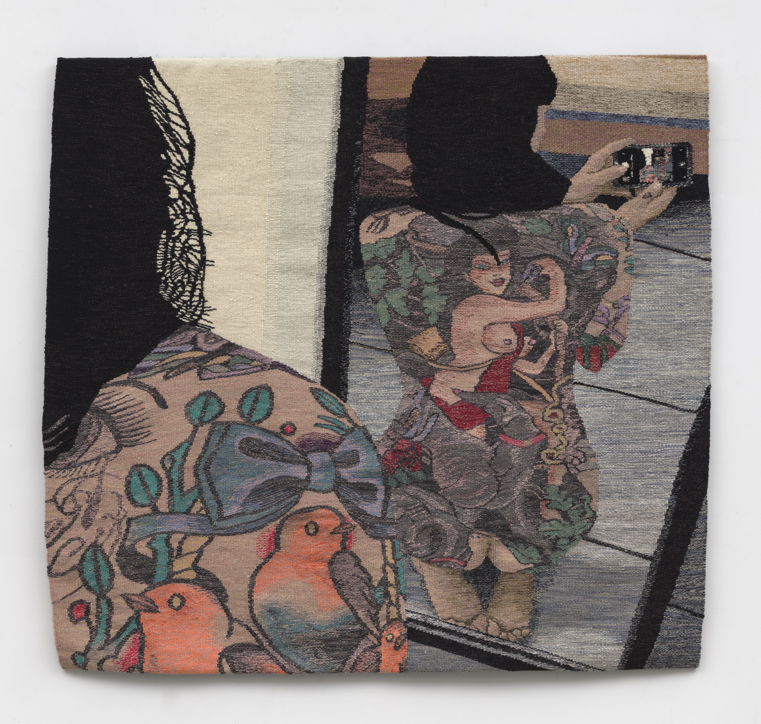 Woven tapestry of a woman with dark hair and full-body tattoos kneeling with her back to a mirror, taking a picture with a cell phone over her shoulder.
