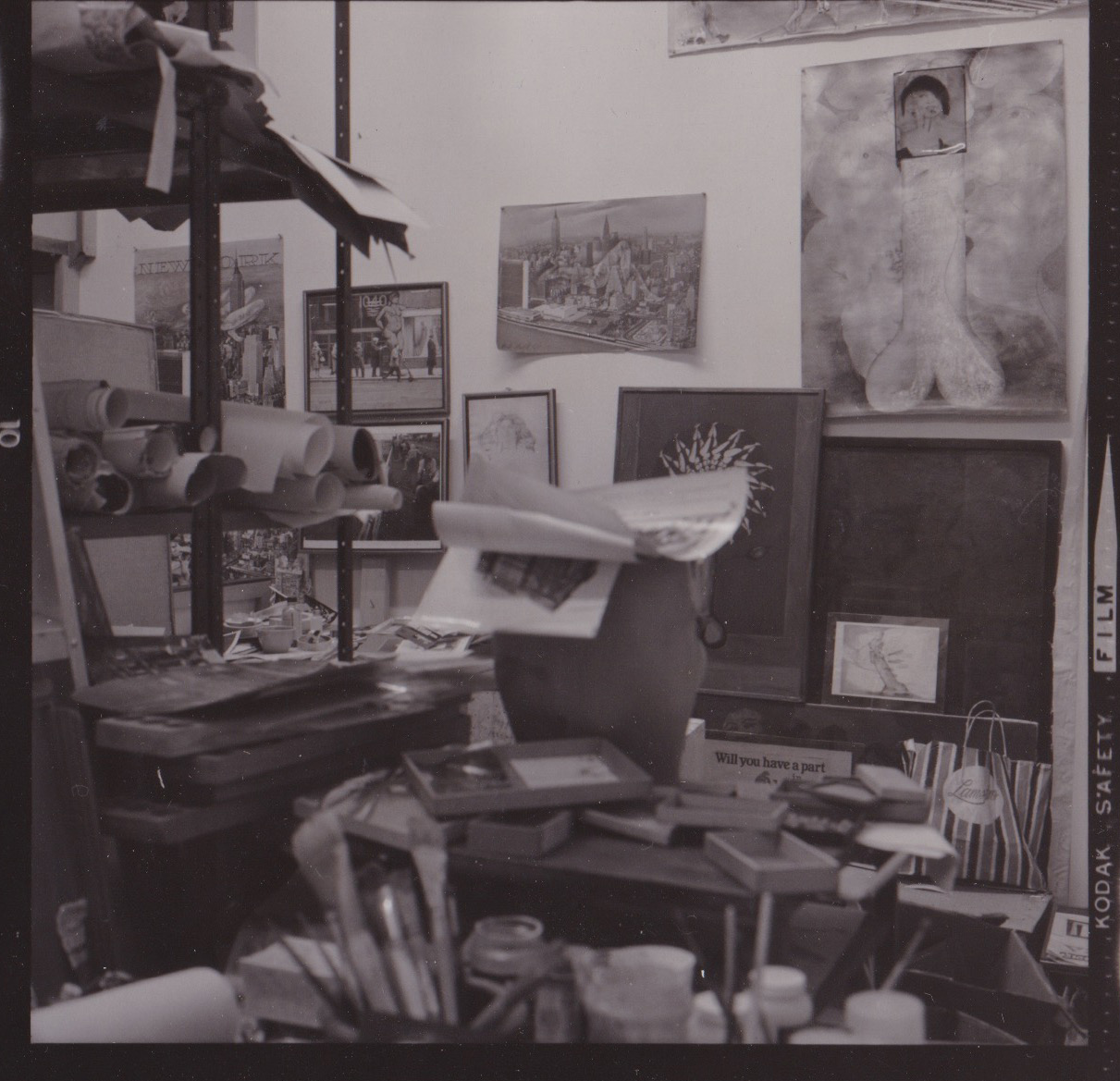 Black-and-white photograph of a cluttered artist's studio. Hanging on the wall to the right is a large painting of a phallus.