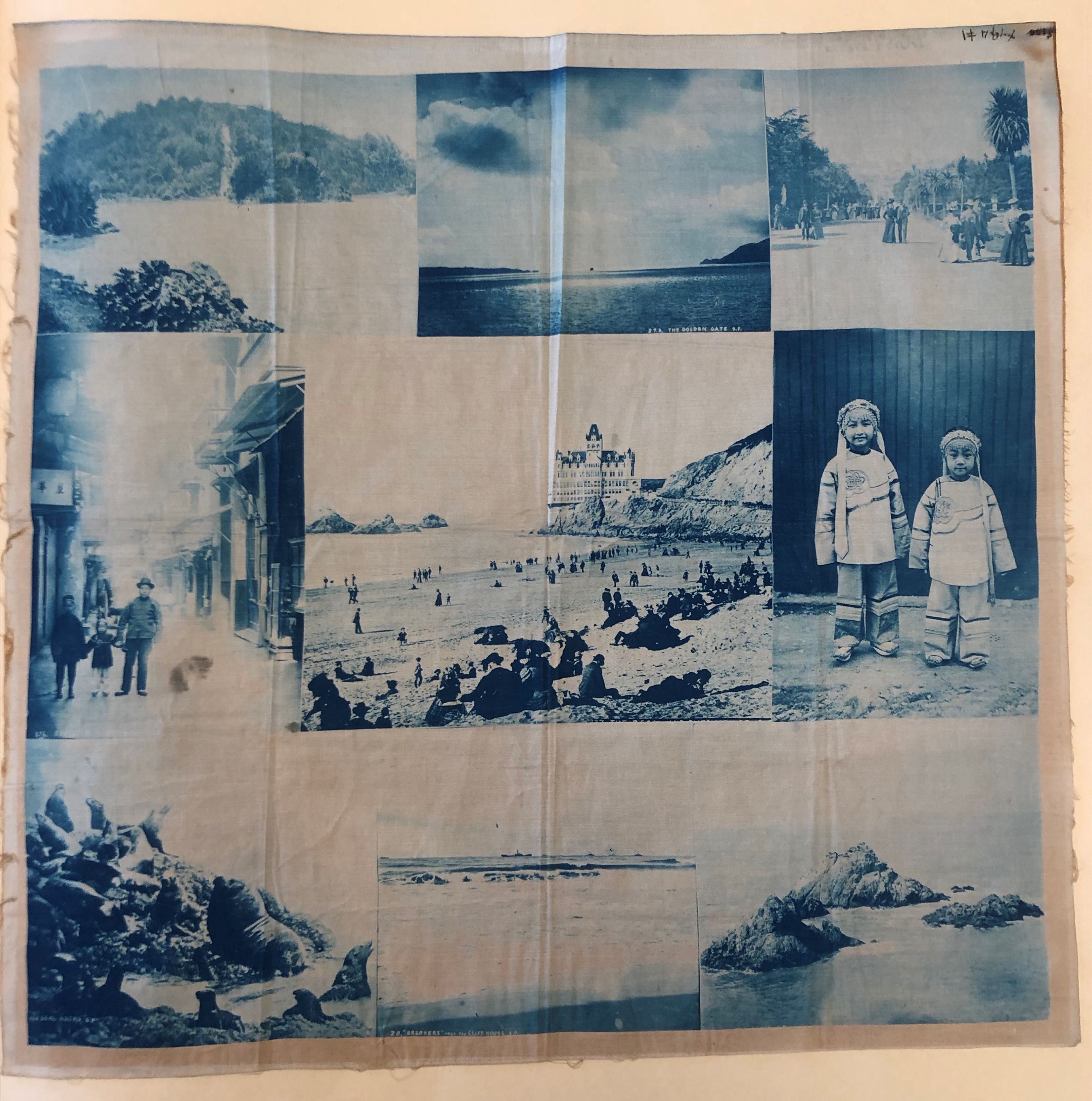 Square piece of fabric printed with nine different photographs in a blue tint. In the center is a view of people on a beach with a castle-like building beyond, flanked on either side by pictures of Asian American families.
