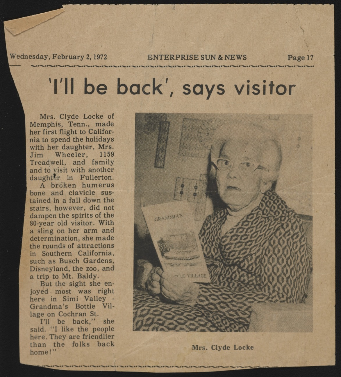 Newspaper clipping dated Wednesday, February 2, 1972 from the "Enterprise Sun & News," p. 17, showing a photograph of an elderly woman holding a brochure reading "Grandma's Bottle Village." The headline reads "'I'll be back', says visitor"