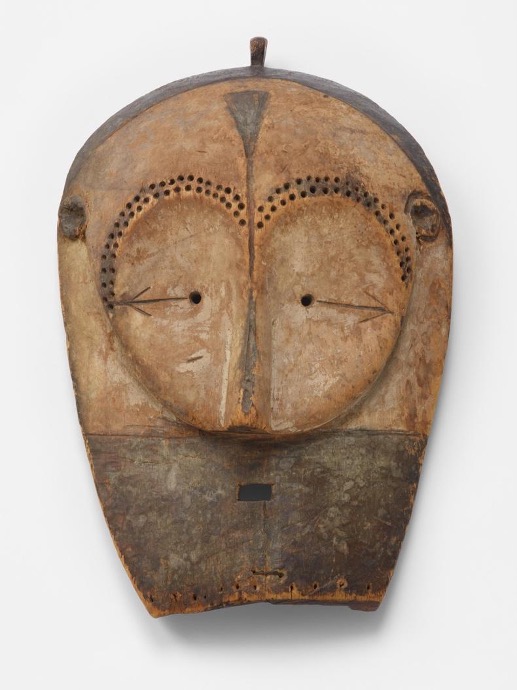 carved wooden mask with minimal features, surrounded by a heart shape made of small holes