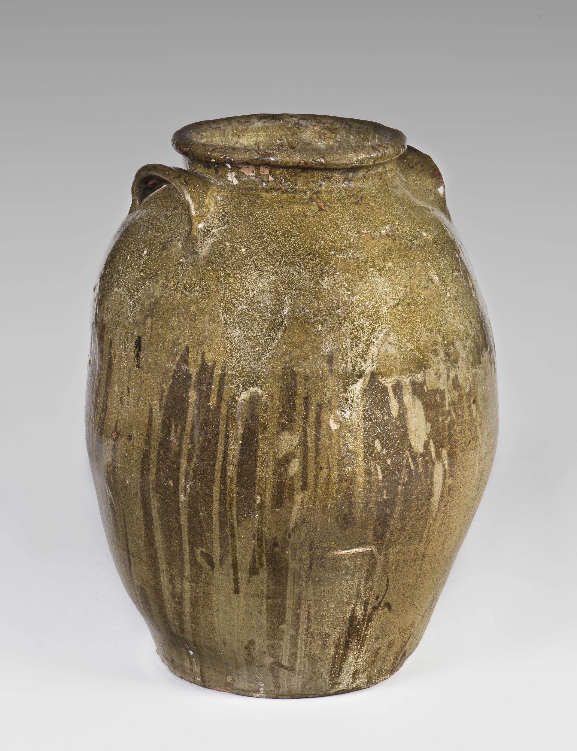 Ceramic vessel with medium-sized mouth and two spoon-shaped handles. The vessel's rough exterior is covered with drips of glaze that vary from cream-colored to brown.