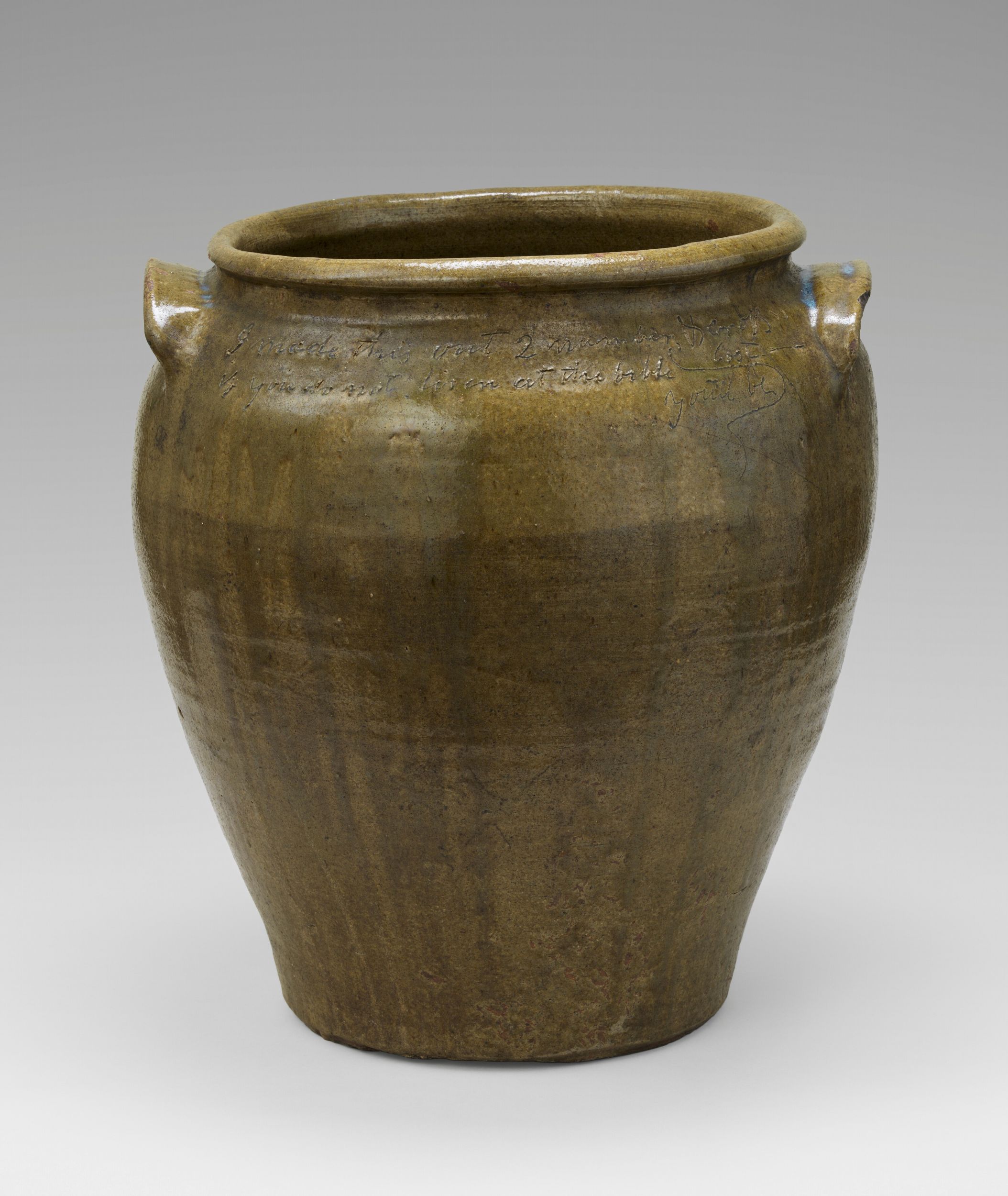 Ceramic vessel with a wide mouth and two ear-shaped handles. The vessel has a rough brown glaze and an inscription near the top, illegible in this photograph.