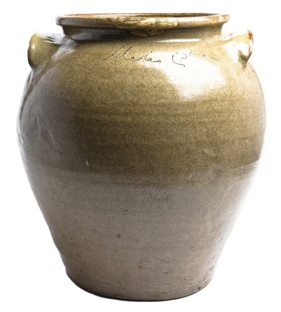 Ceramic vessel with a wide mouth and two spoon-shaped handles. The exterior is covered with brown glaze and shows horizontal striations. Near the rim is an inscription that is illegible in this photograph.