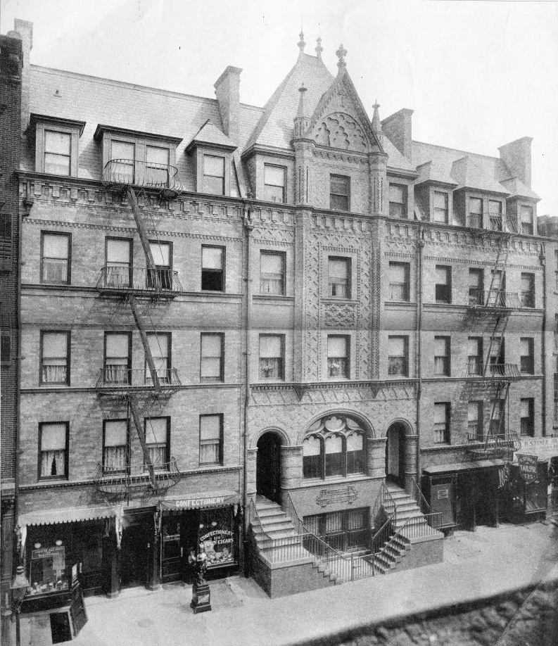 Black-and-white photograph of a city block, with a gothic facade in the middle, flanked by a double stairway.