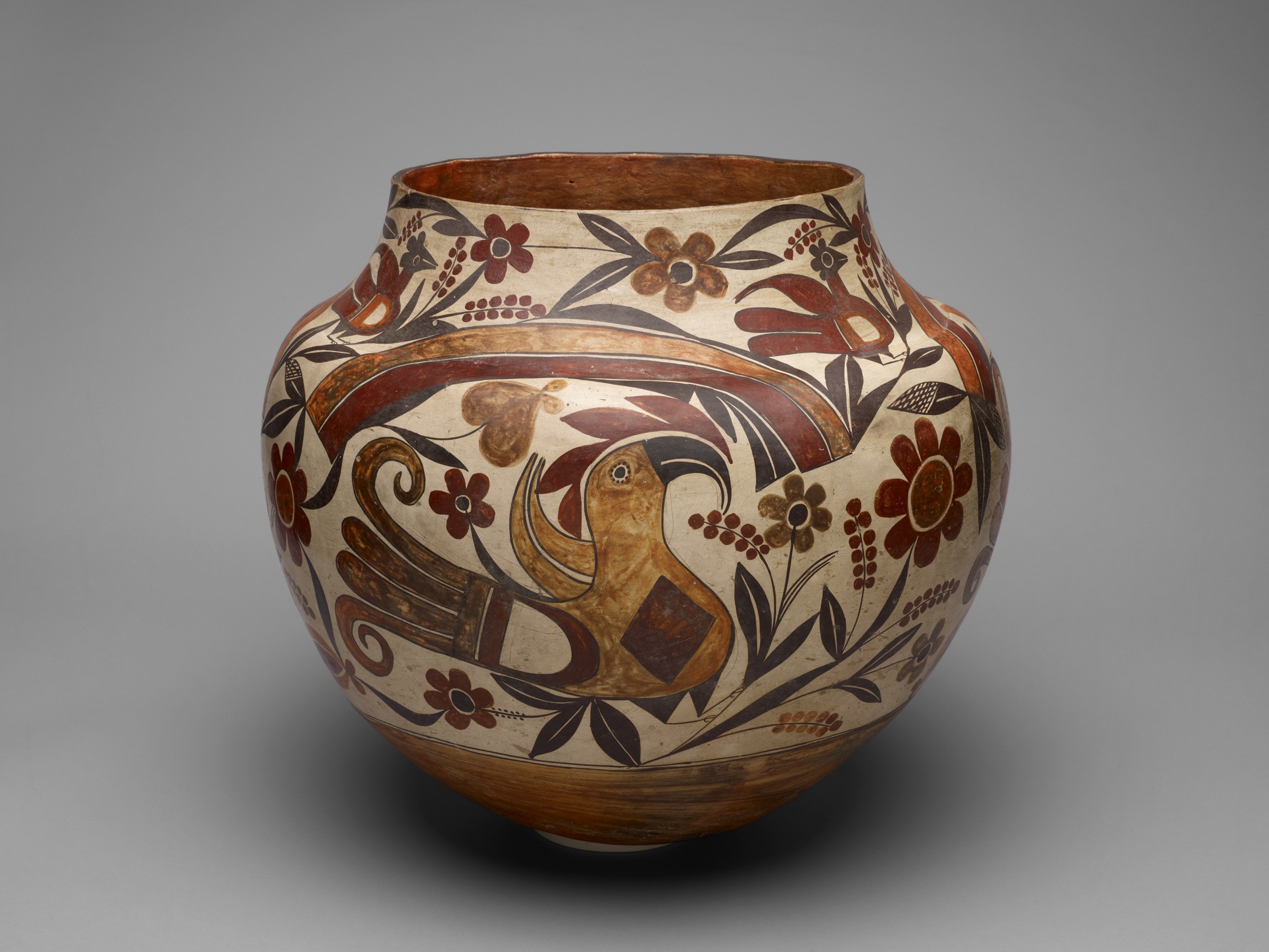 Ceramic jar with a globe-shaped body and a narrower, tapered rim. The decoration is in tones of cream, brown, and ocher and shows a bird with a large beak, flowers, and a swooping striped design.