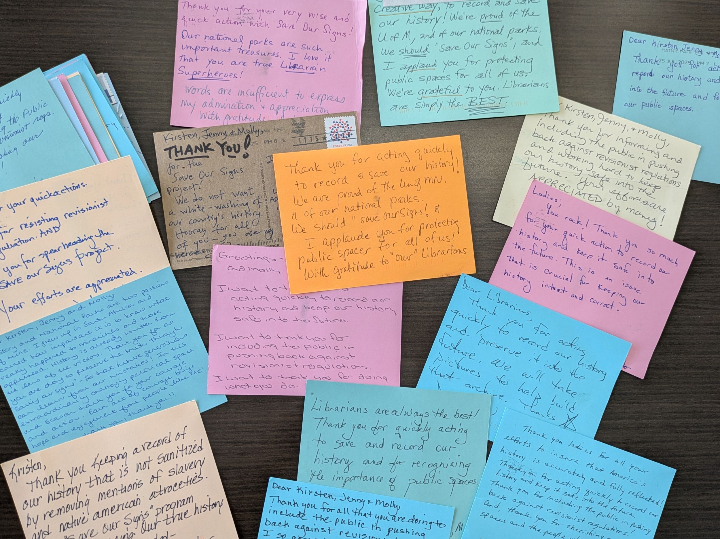 Overhead view of a desktop covered with solid-colored postcards handwritten with messages of thanks.