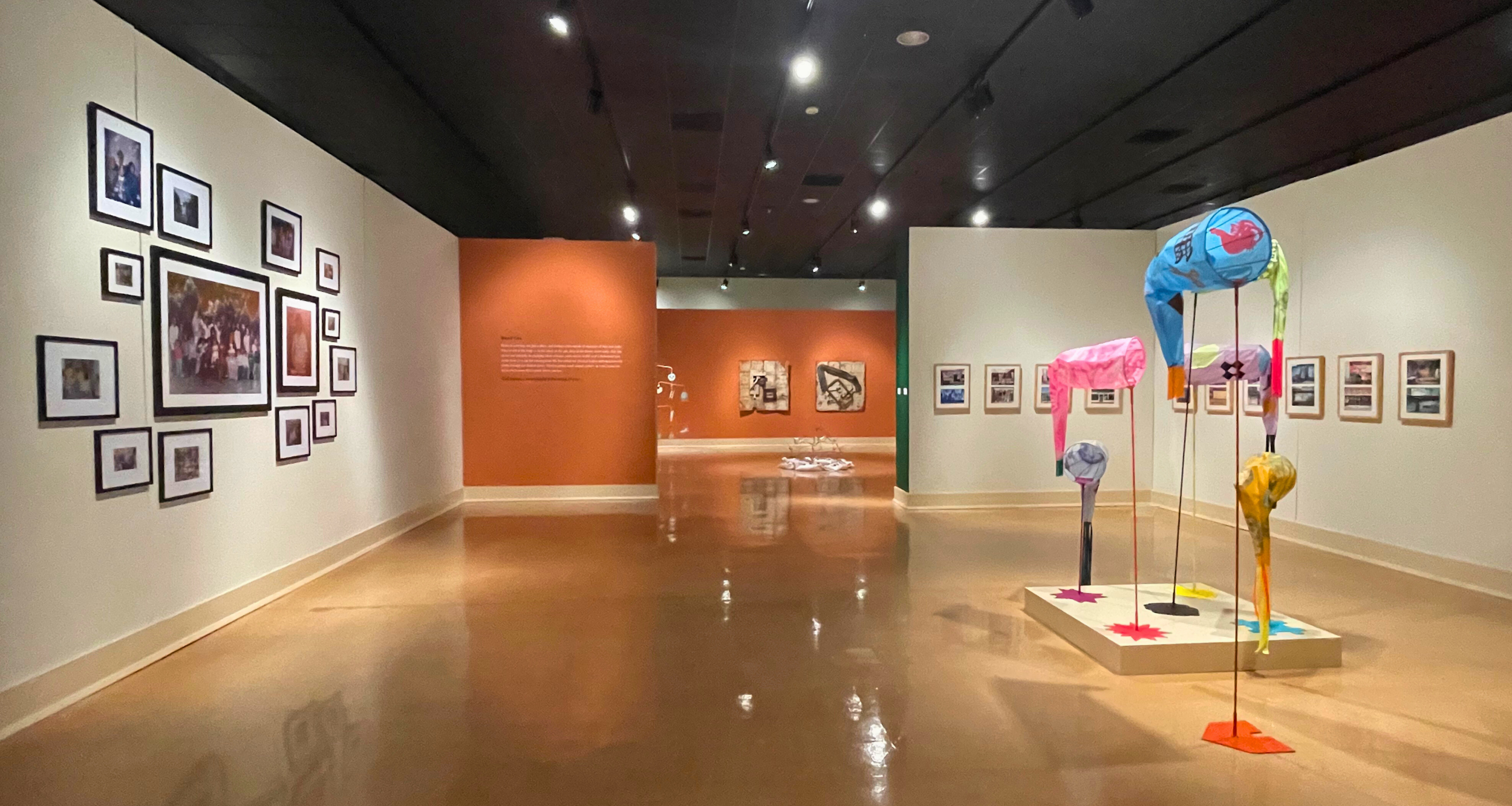 Interior of museum gallery with framed works on the walls and a large, colorful, abstract sculpture on the floor to the right.