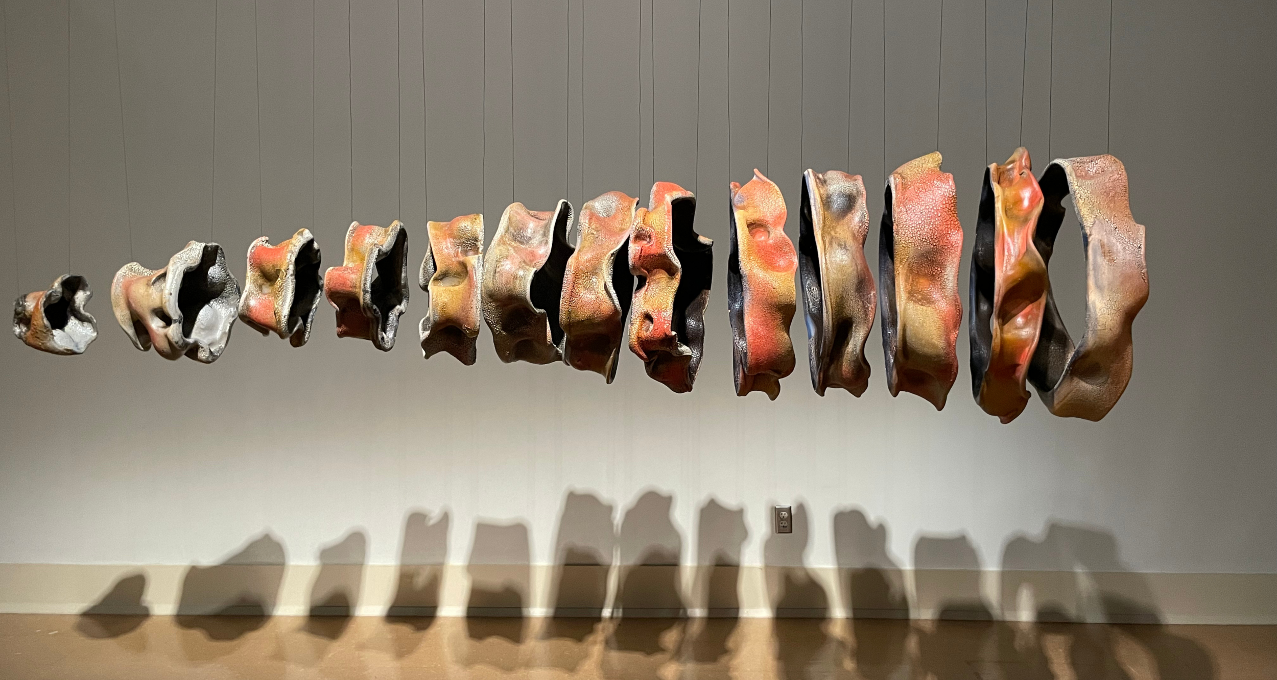 Sculptural work consisting of several circlets of irregularly shaped ceramic, suspended from black filaments and arranged in order of size, smallest on the left.