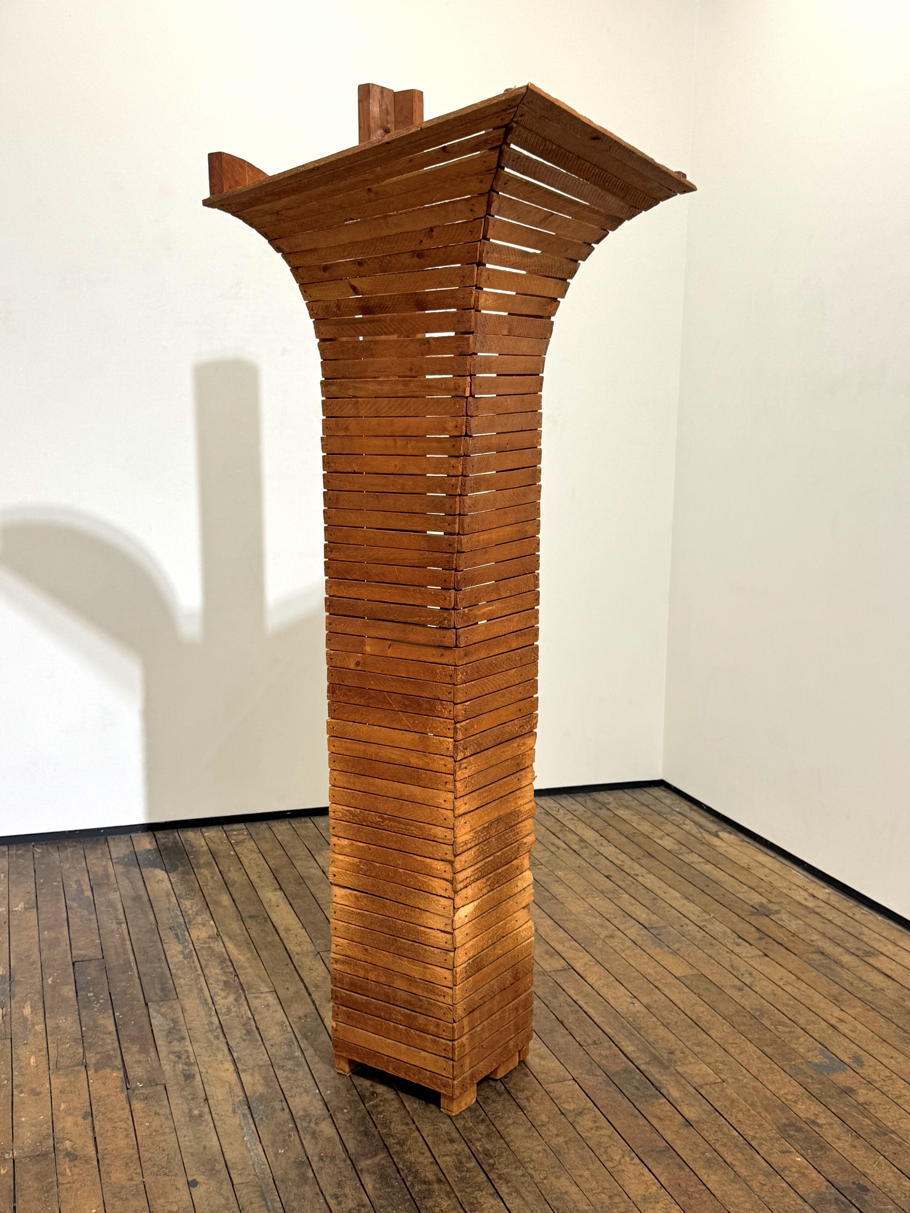Large wooden sculpture in a gallery setting. The sculpture is curved at the top and composed of wooden slats.
