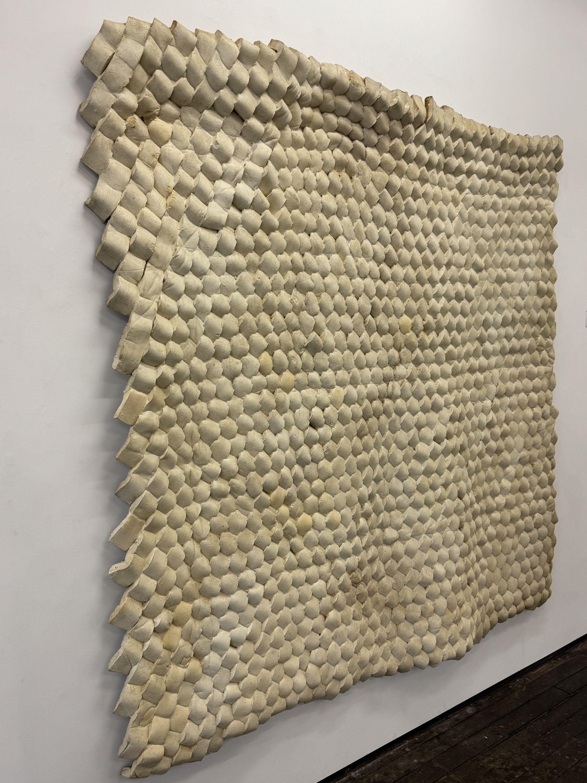 Wall hanging composed of woven chunks of synthetic material, a dirty white color in appearance.