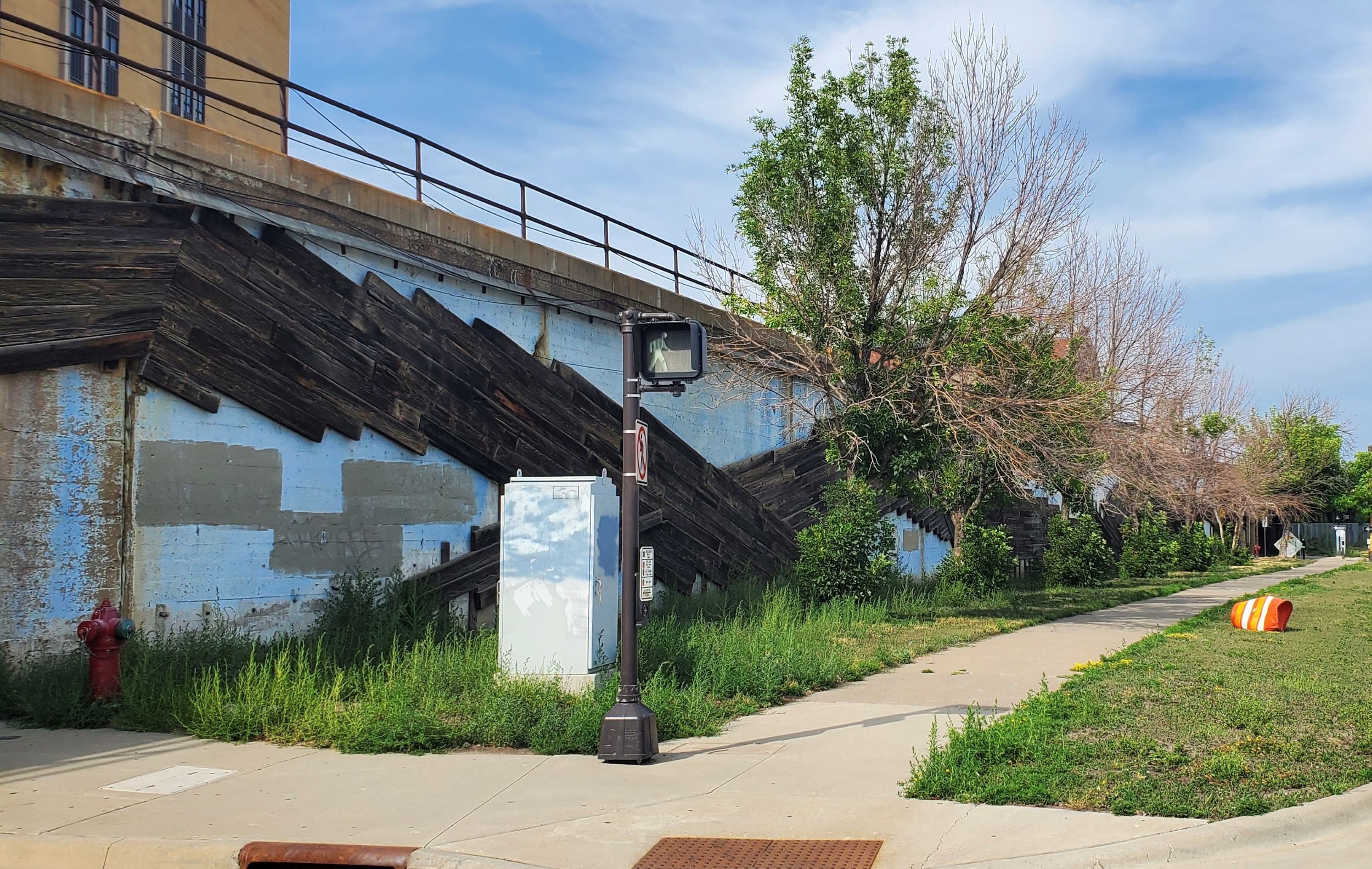 Urban street view showing a fragment of the mural in fig. 1, now in disrepair, surrounded by untended greenery.