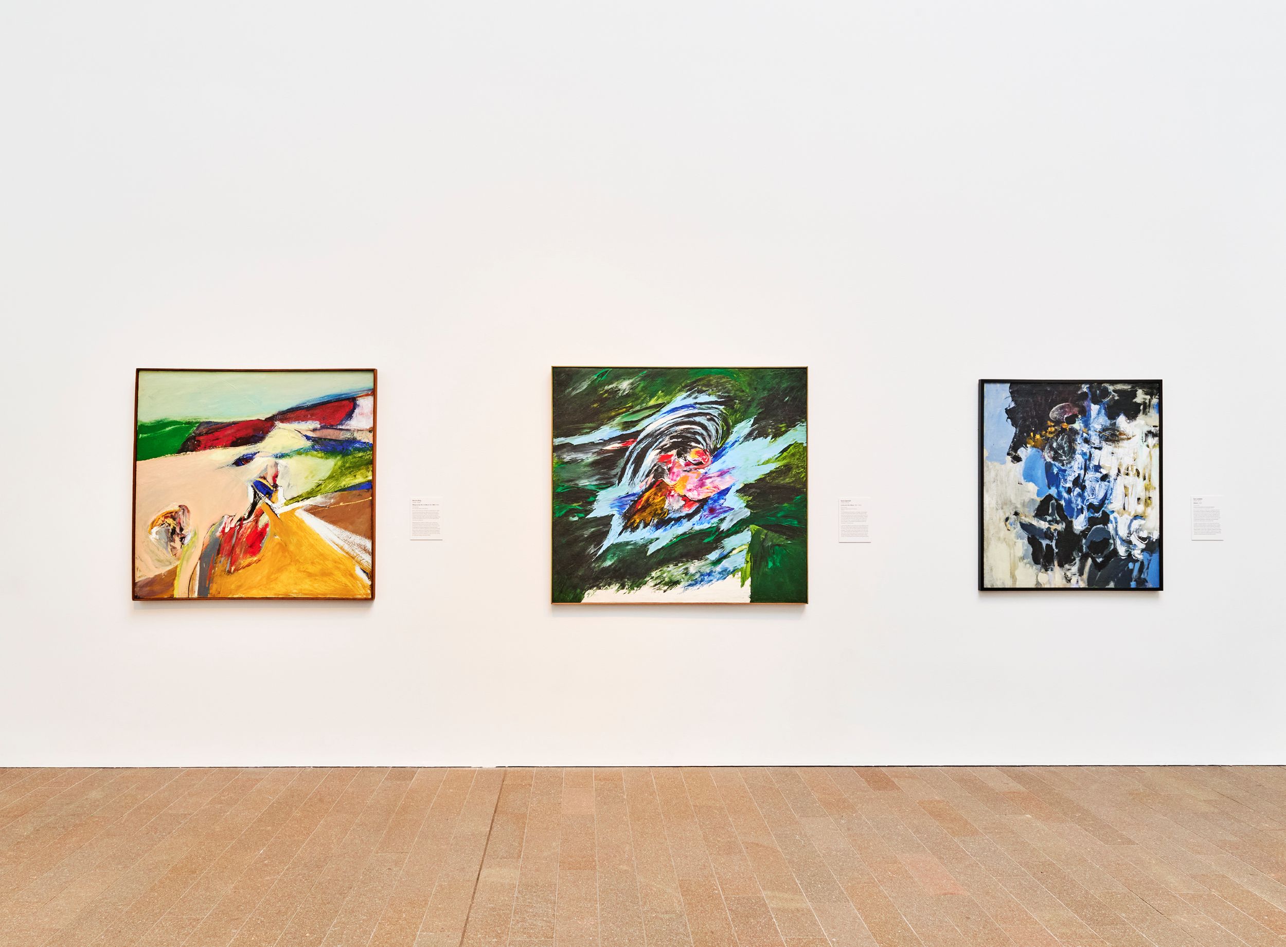 Head on view of gallery wall with three colorful, abstract paintings hung in a row.
